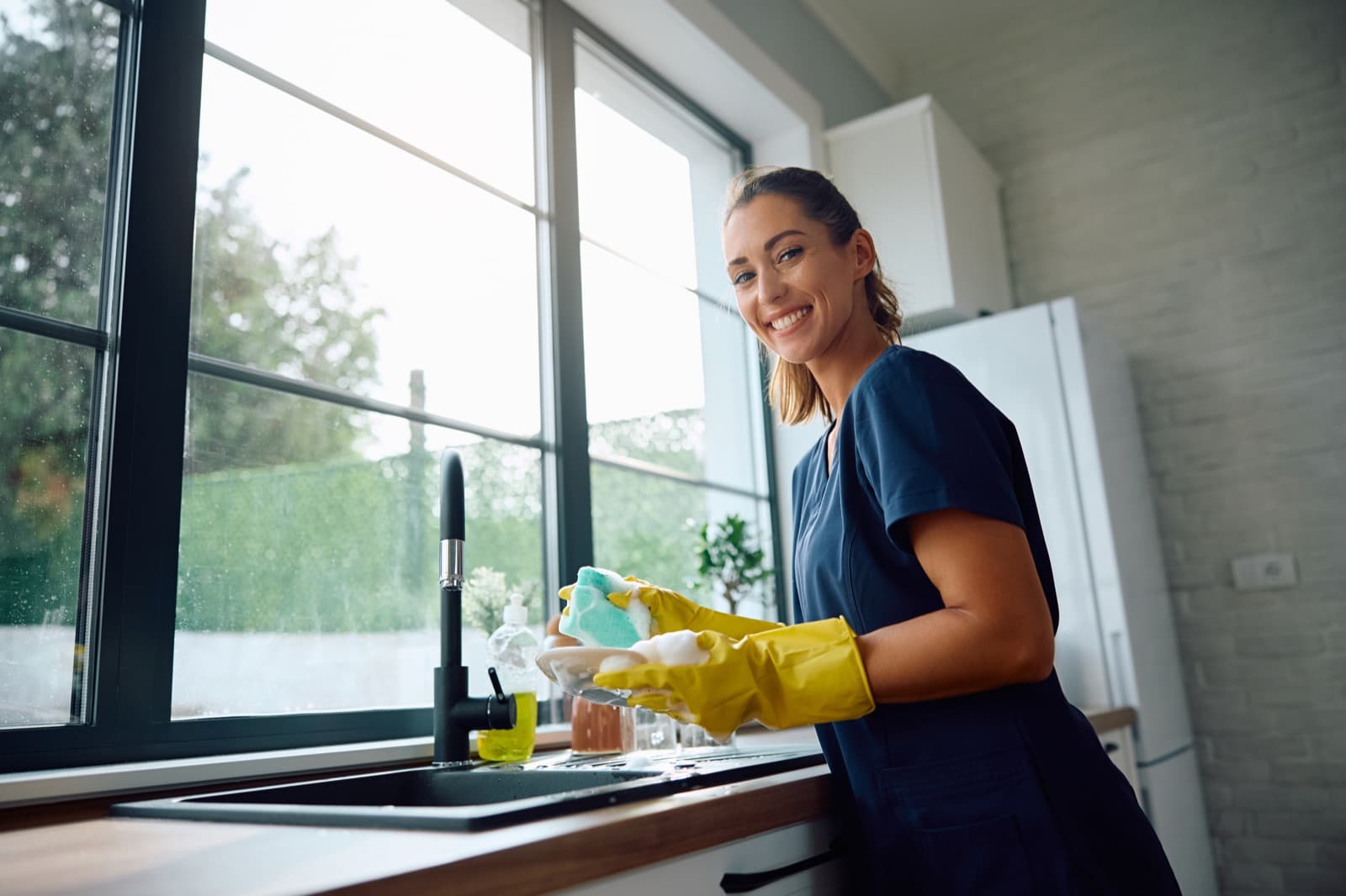 Professional cleaner washing dishes in a bright modern kitchen