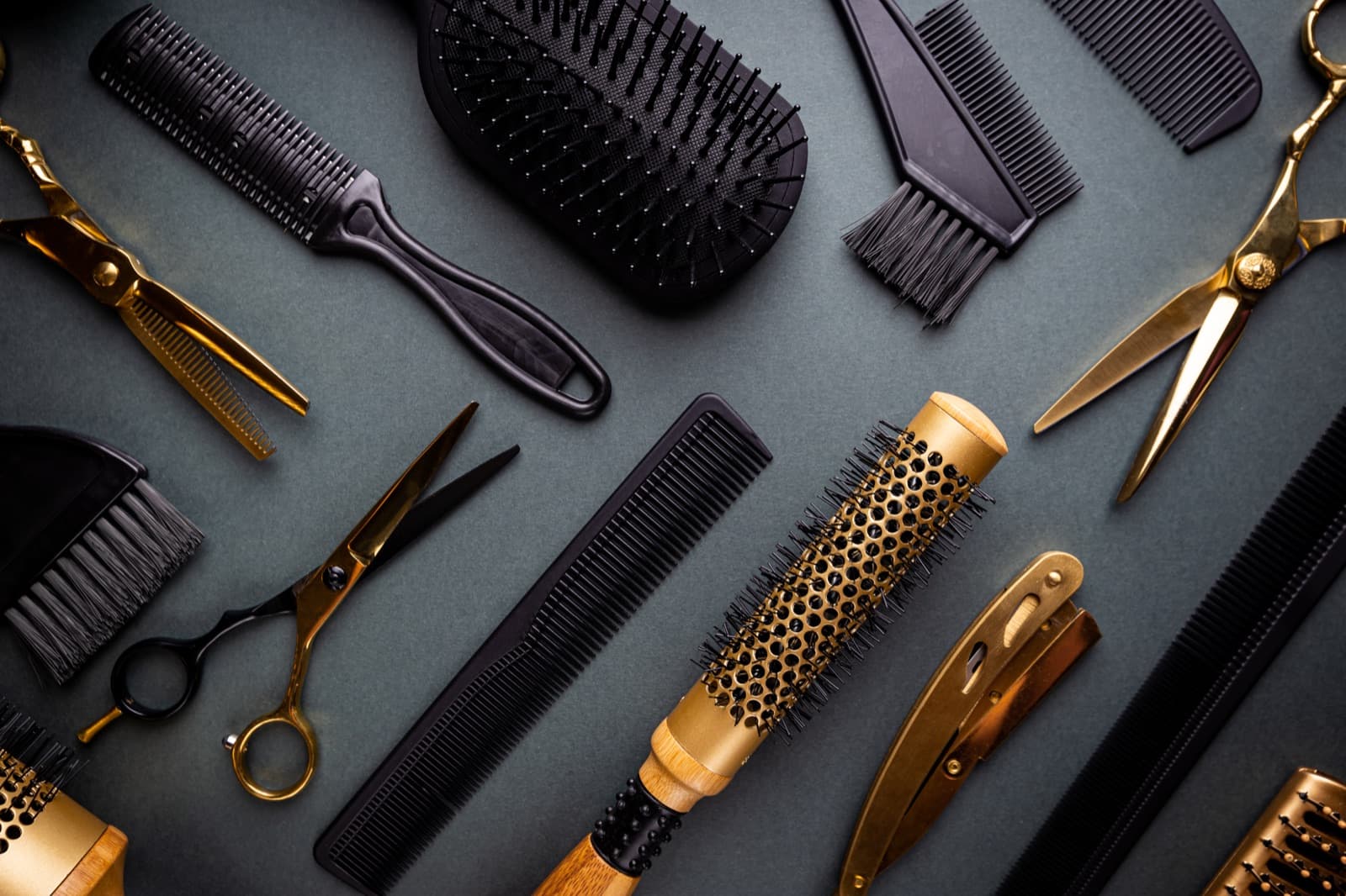 Professional brushes, combs, and gold hair-cutting shears arranged on a dark surface