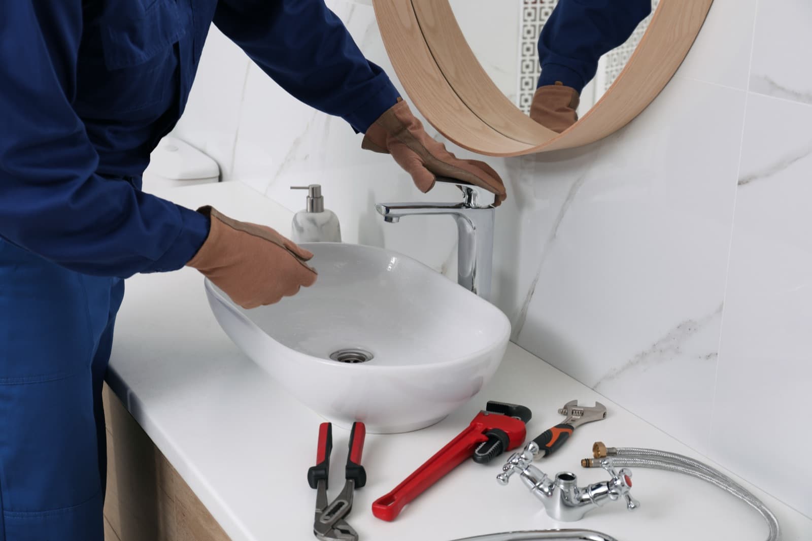 Plumber checking a modern bathroom sink with repair tools ready on the counter