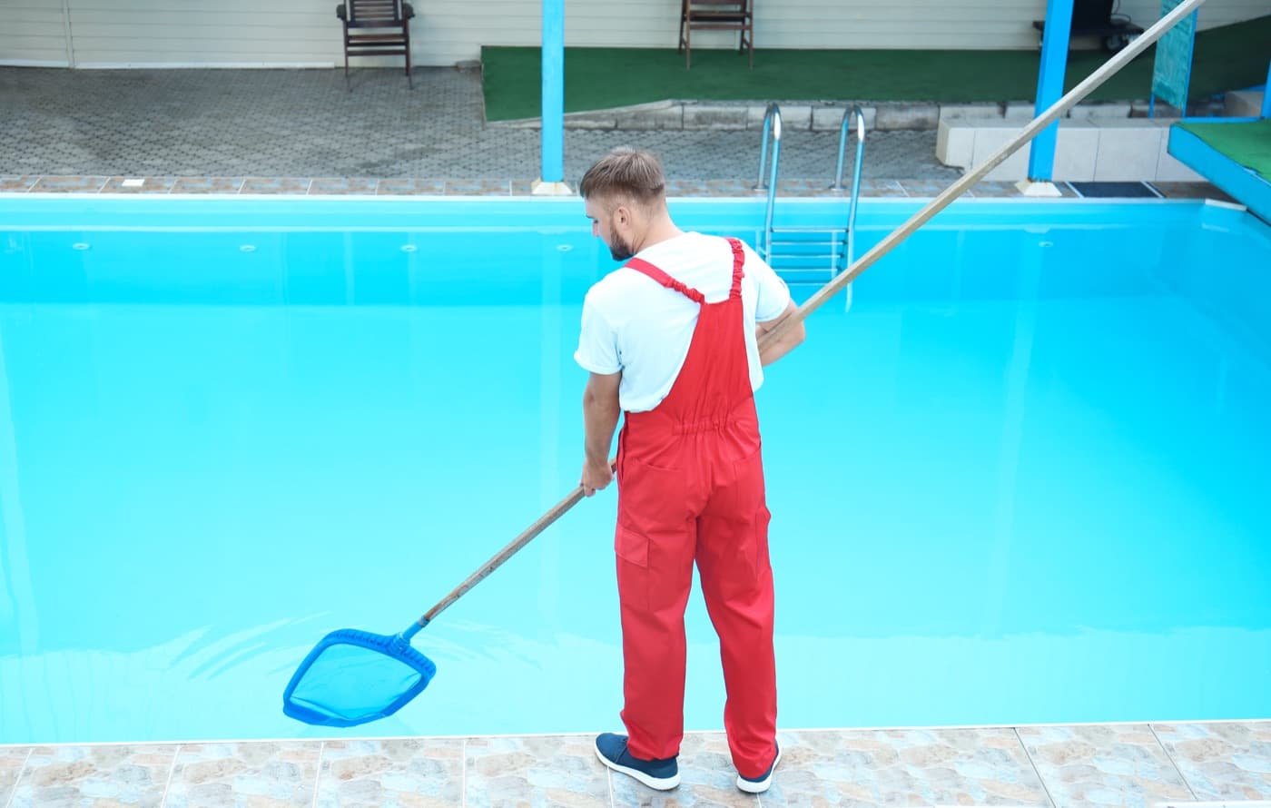 Pool-service worker cleaning an outdoor swimming pool with a scoop net