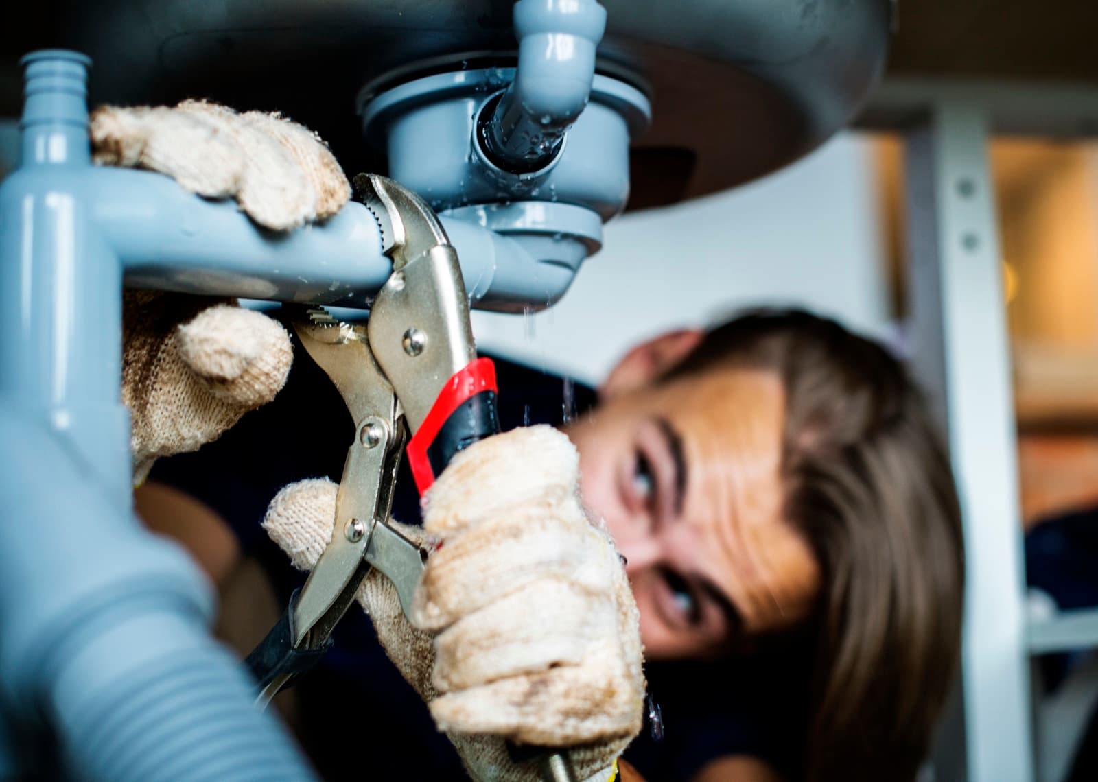 Plumber tightening a leaking pipe under a sink